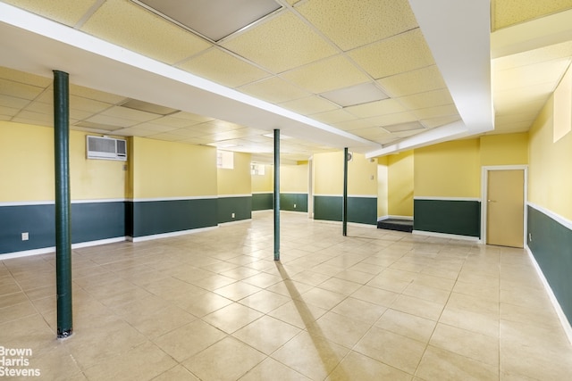 basement featuring tile patterned floors, a wall mounted air conditioner, and a drop ceiling