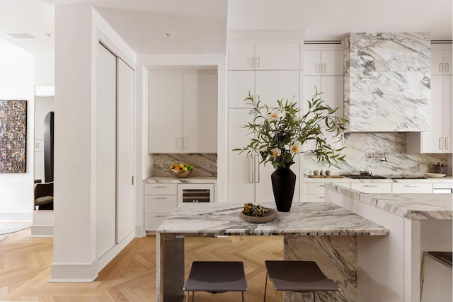 kitchen with light stone countertops, white cabinetry, wine cooler, decorative backsplash, and light parquet floors