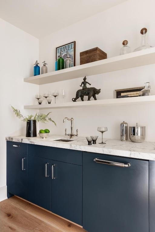 bar featuring blue cabinets, light stone counters, and light hardwood / wood-style flooring