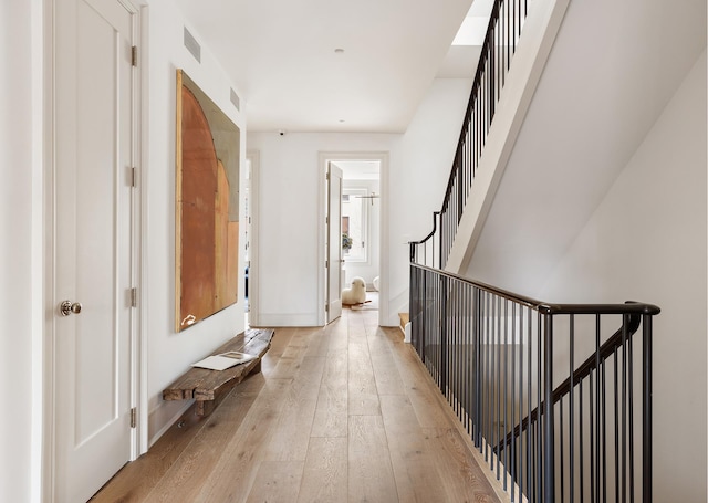 corridor with baseboards, visible vents, light wood finished floors, and stairs