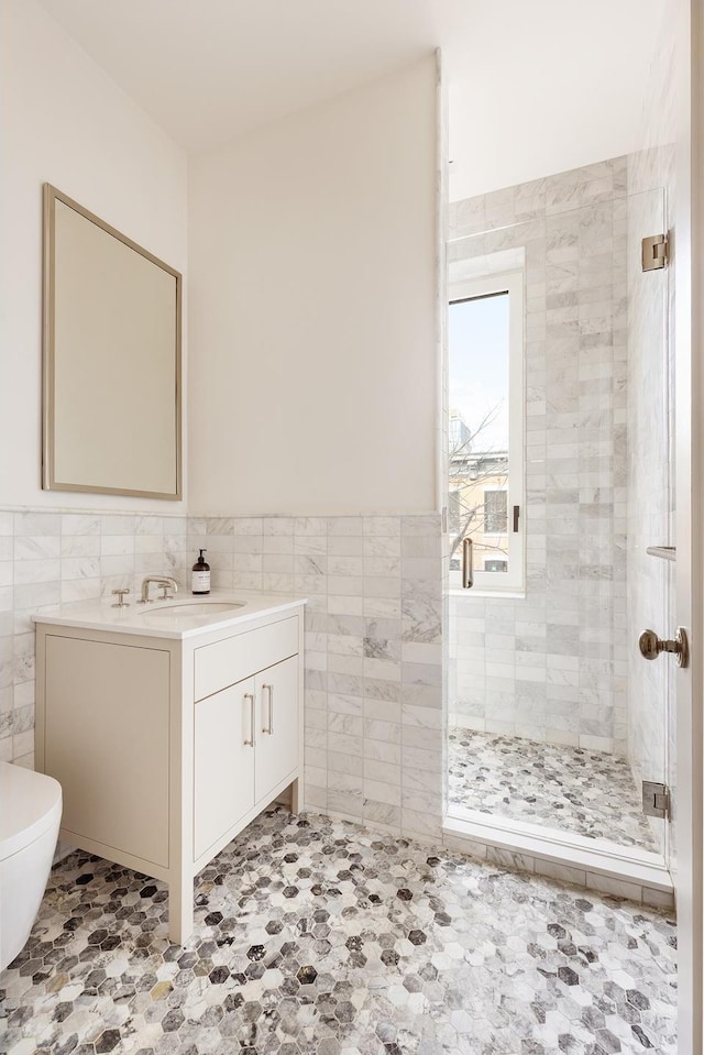 full bath with toilet, vanity, a shower stall, and tile walls