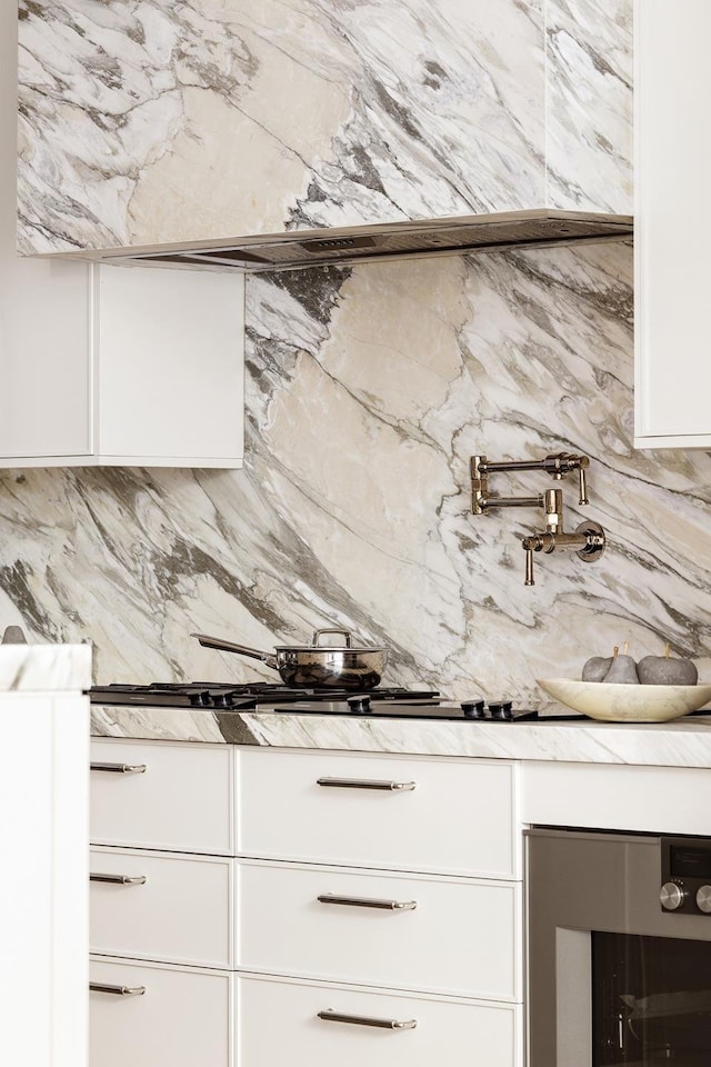 kitchen with tasteful backsplash, beverage cooler, white cabinets, and light stone countertops