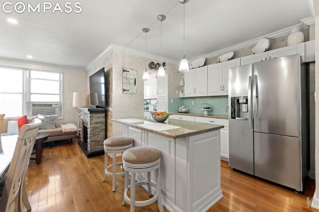 kitchen with white cabinetry, stainless steel refrigerator with ice dispenser, decorative light fixtures, a kitchen breakfast bar, and light stone countertops