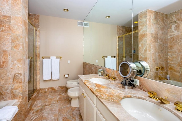 bathroom with toilet, vanity, tile walls, a bidet, and a shower with door