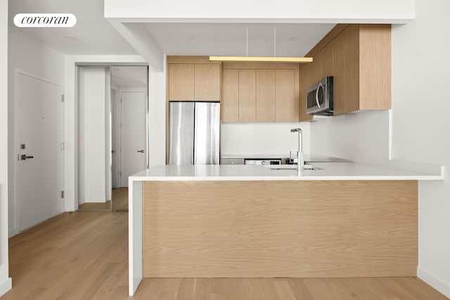 kitchen featuring stainless steel appliances, a peninsula, a sink, light countertops, and light wood-type flooring