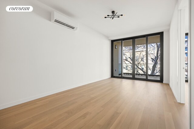 spare room featuring a wall of windows, an AC wall unit, light wood-style flooring, and baseboards