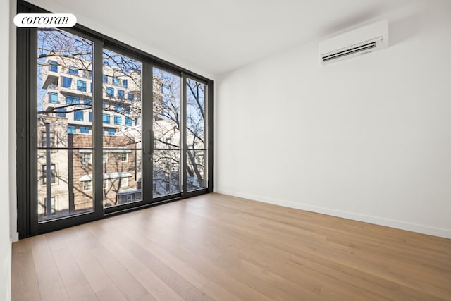 spare room with an AC wall unit, wood-type flooring, and expansive windows