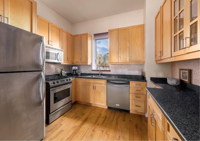 kitchen featuring sink, stainless steel appliances, decorative backsplash, dark stone counters, and light wood-type flooring