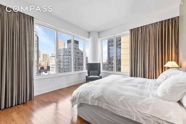 bedroom with a view of city, baseboards, and wood finished floors