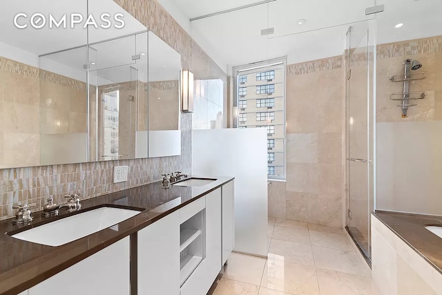 bathroom featuring a sink, tile walls, a shower stall, and double vanity