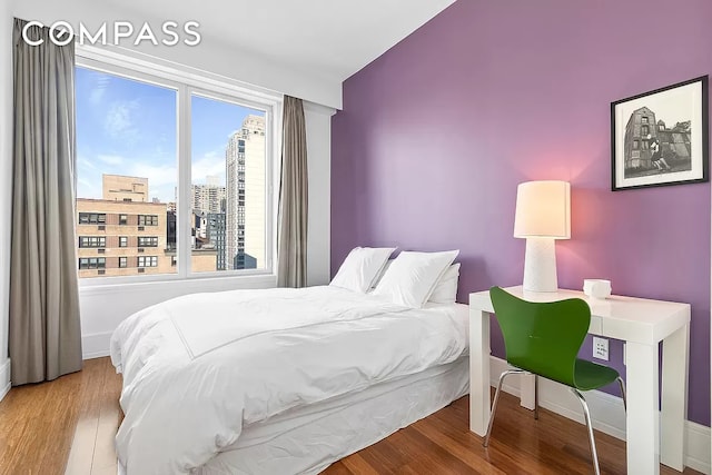 bedroom with a city view, baseboards, and wood finished floors