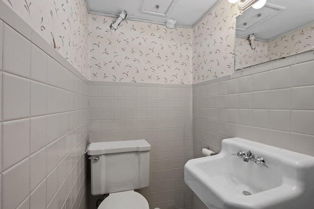 bathroom featuring a wainscoted wall, a sink, toilet, and wallpapered walls