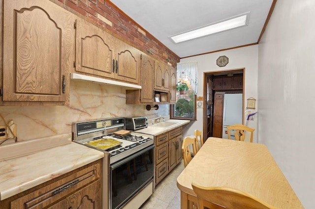 kitchen featuring white gas range, light countertops, crown molding, under cabinet range hood, and backsplash