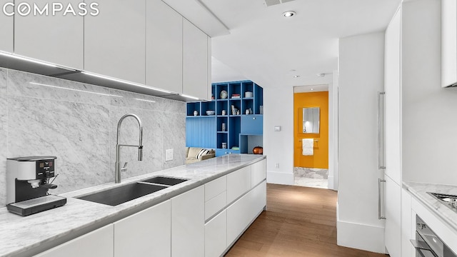 kitchen with tasteful backsplash, white cabinetry, sink, light hardwood / wood-style floors, and light stone countertops