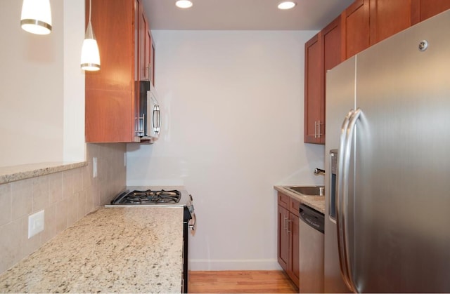 kitchen with sink, stainless steel appliances, pendant lighting, and light stone countertops