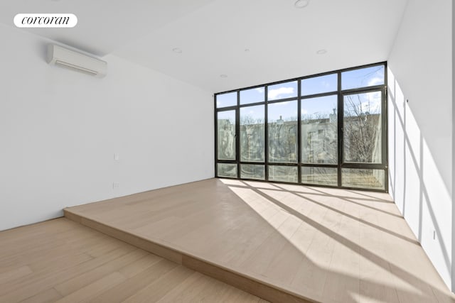 unfurnished room with a wall unit AC, light wood-style floors, visible vents, and floor to ceiling windows