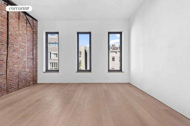 empty room featuring brick wall, light wood finished floors, and a healthy amount of sunlight