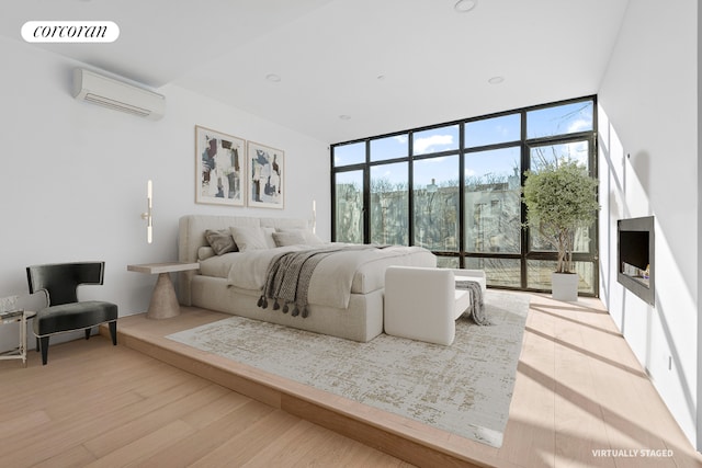 bedroom with an AC wall unit, light wood-style floors, multiple windows, and floor to ceiling windows