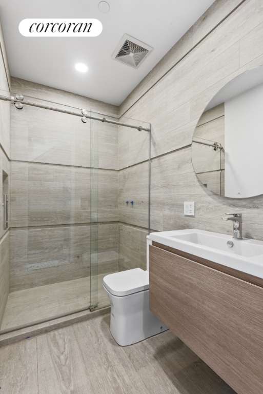 bathroom with toilet, wood finished floors, vanity, visible vents, and a shower stall