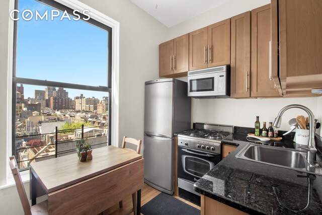 kitchen featuring stainless steel appliances, light hardwood / wood-style floors, sink, and dark stone countertops