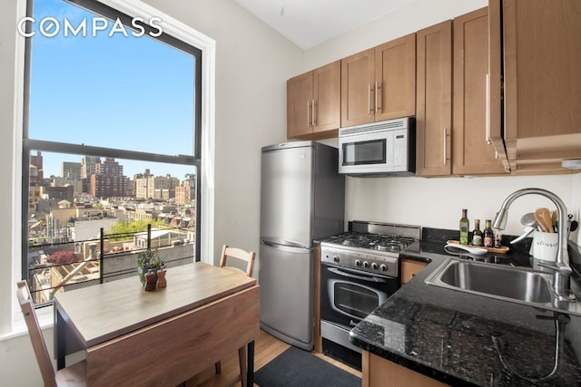 kitchen with appliances with stainless steel finishes, sink, light hardwood / wood-style flooring, and dark stone counters