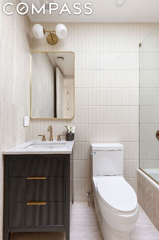 full bathroom featuring toilet, tile walls, vanity, and tiled shower / bath combo