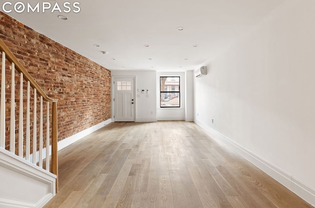 unfurnished room featuring a wall mounted air conditioner, brick wall, and light wood-type flooring