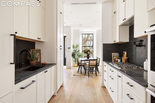 kitchen with white cabinetry, sink, backsplash, stainless steel gas stovetop, and light hardwood / wood-style flooring