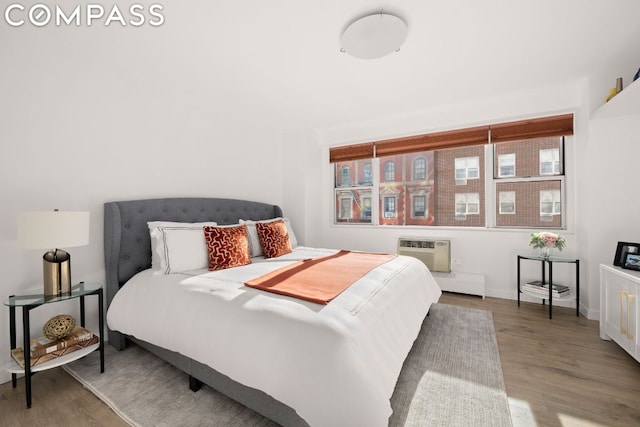 bedroom featuring a baseboard heating unit, hardwood / wood-style flooring, and a wall mounted AC