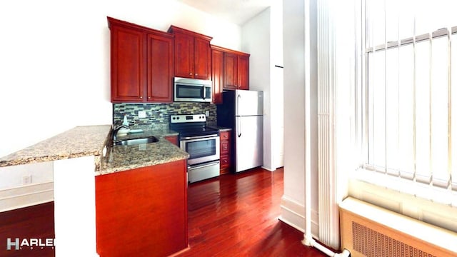 kitchen featuring a sink, appliances with stainless steel finishes, backsplash, radiator heating unit, and dark wood finished floors