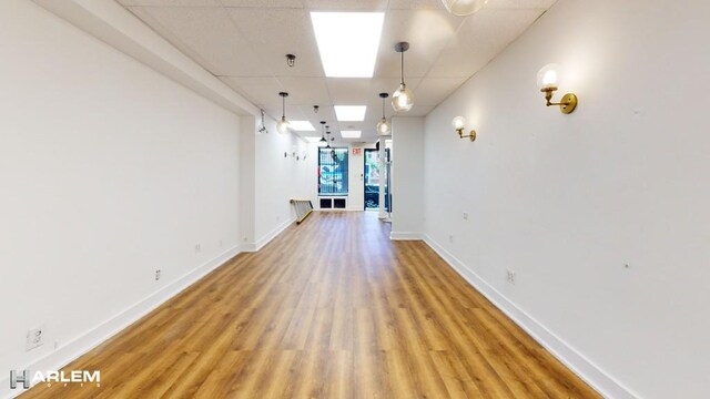 empty room featuring a paneled ceiling, light wood-style flooring, and baseboards