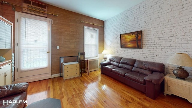 living room featuring brick wall, a healthy amount of sunlight, a wall unit AC, and light wood-type flooring