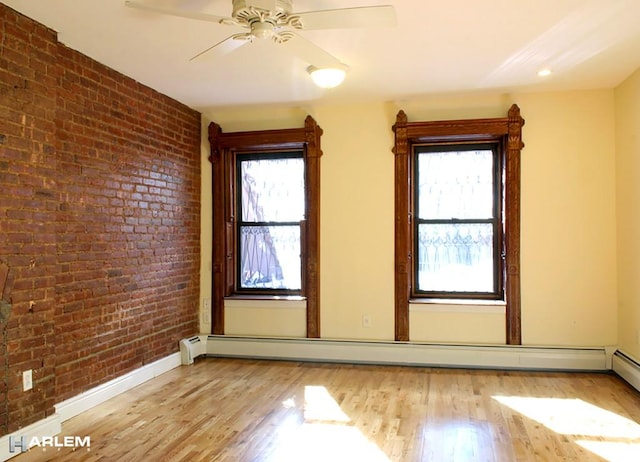 spare room with light hardwood / wood-style flooring, a wealth of natural light, a baseboard radiator, and brick wall