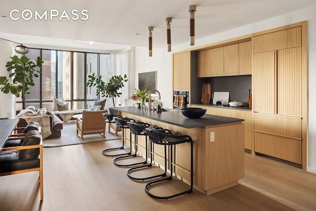 kitchen featuring dark countertops, open floor plan, a center island with sink, and light wood-style flooring