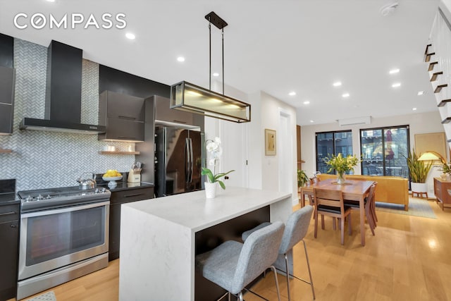 kitchen featuring light wood finished floors, freestanding refrigerator, wall chimney range hood, modern cabinets, and stainless steel range with electric stovetop