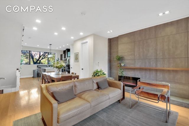 living room featuring baseboards, light wood-type flooring, a fireplace, and recessed lighting