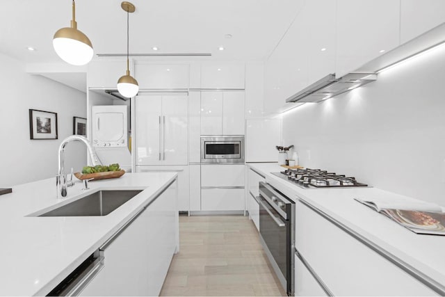 kitchen with white cabinetry, stainless steel appliances, decorative light fixtures, sink, and stacked washer and clothes dryer