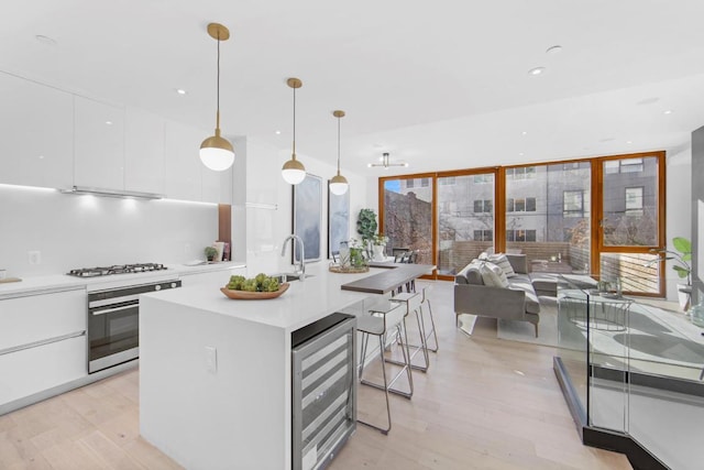 kitchen featuring wine cooler, white gas cooktop, hanging light fixtures, wall oven, and white cabinets