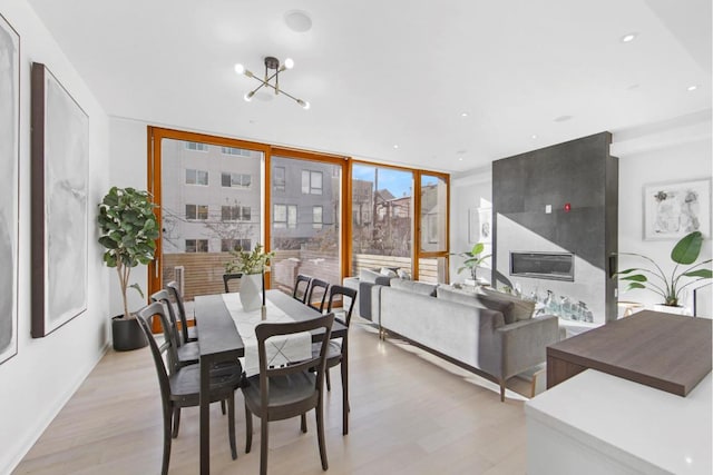 dining space with light hardwood / wood-style floors, a chandelier, a large fireplace, and floor to ceiling windows