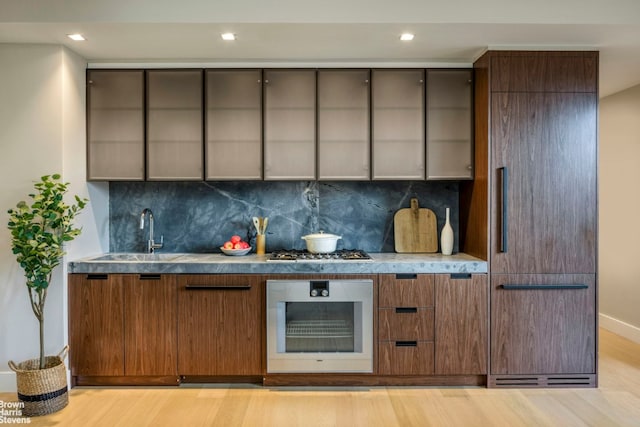 bar with sink, backsplash, appliances with stainless steel finishes, and light hardwood / wood-style flooring