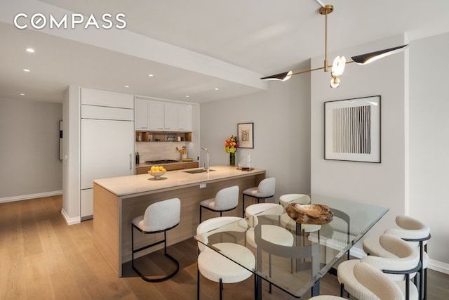 kitchen featuring a sink, a kitchen breakfast bar, light wood-style flooring, a peninsula, and white cabinetry