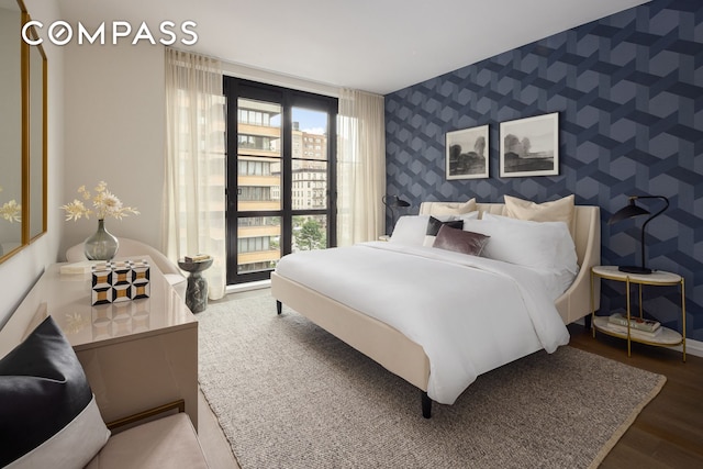 bedroom featuring wallpapered walls, wood finished floors, baseboards, and an accent wall