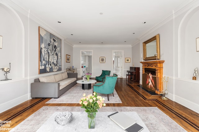 living room with ornamental molding, arched walkways, a warm lit fireplace, and wood finished floors