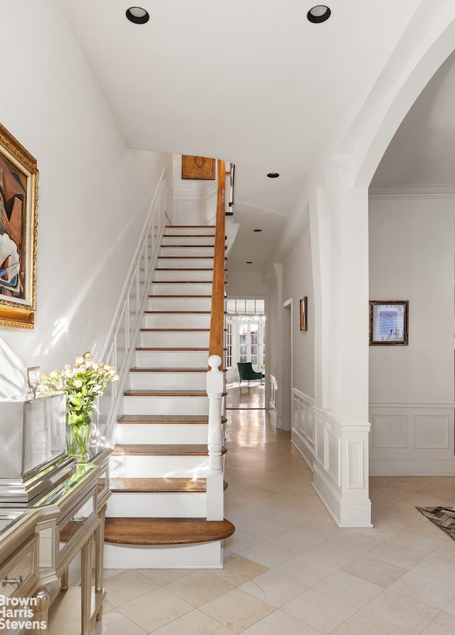 staircase featuring arched walkways, a decorative wall, a wainscoted wall, and recessed lighting