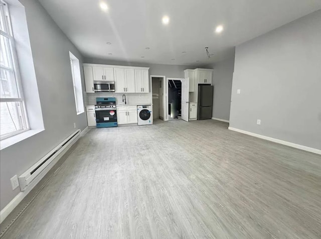 unfurnished living room with a baseboard radiator, washer / clothes dryer, sink, and light hardwood / wood-style flooring