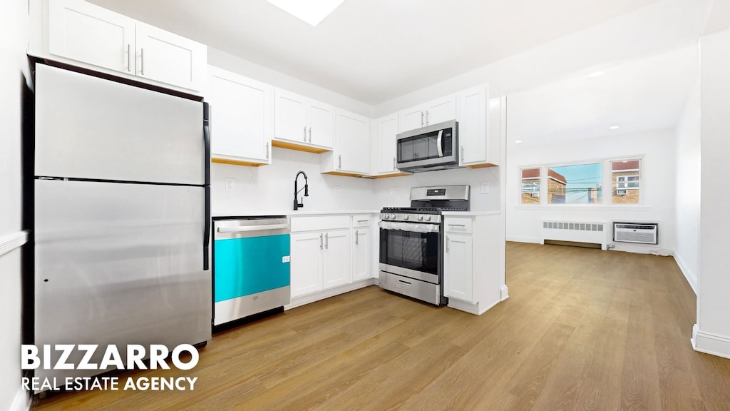 kitchen with light wood-style floors, white cabinets, light countertops, appliances with stainless steel finishes, and radiator