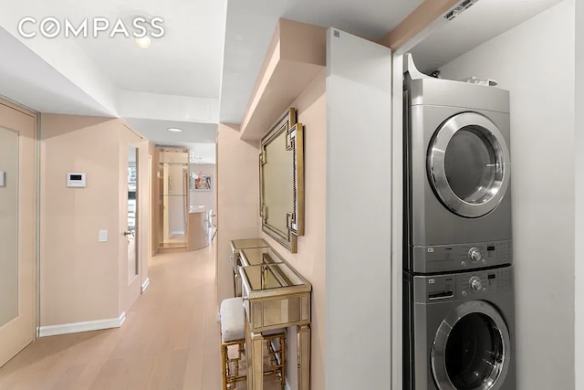 laundry area featuring light wood-style floors, baseboards, laundry area, and stacked washer / dryer