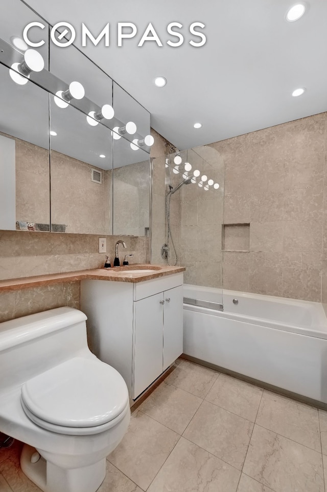 full bath featuring visible vents, vanity, toilet, tile walls, and washtub / shower combination