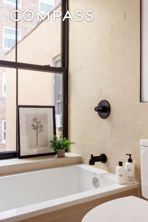 full bath featuring a relaxing tiled tub, toilet, and tiled shower