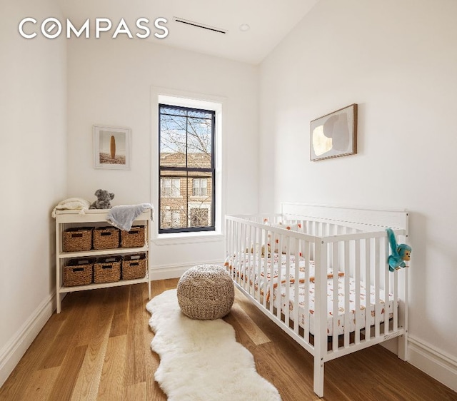 bedroom with a nursery area, baseboards, and wood finished floors